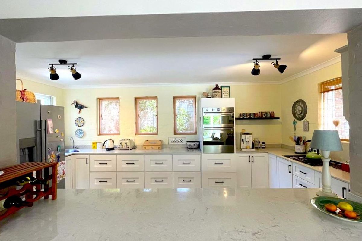 A functional kitchen featuring white cabinetry, stone countertops, built-in oven, and multiple windows providing natural light.