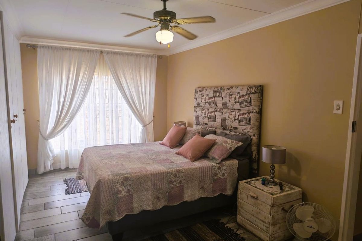 A well-lit bedroom featuring tiled flooring, a ceiling fan, and built-in cupboard storage.