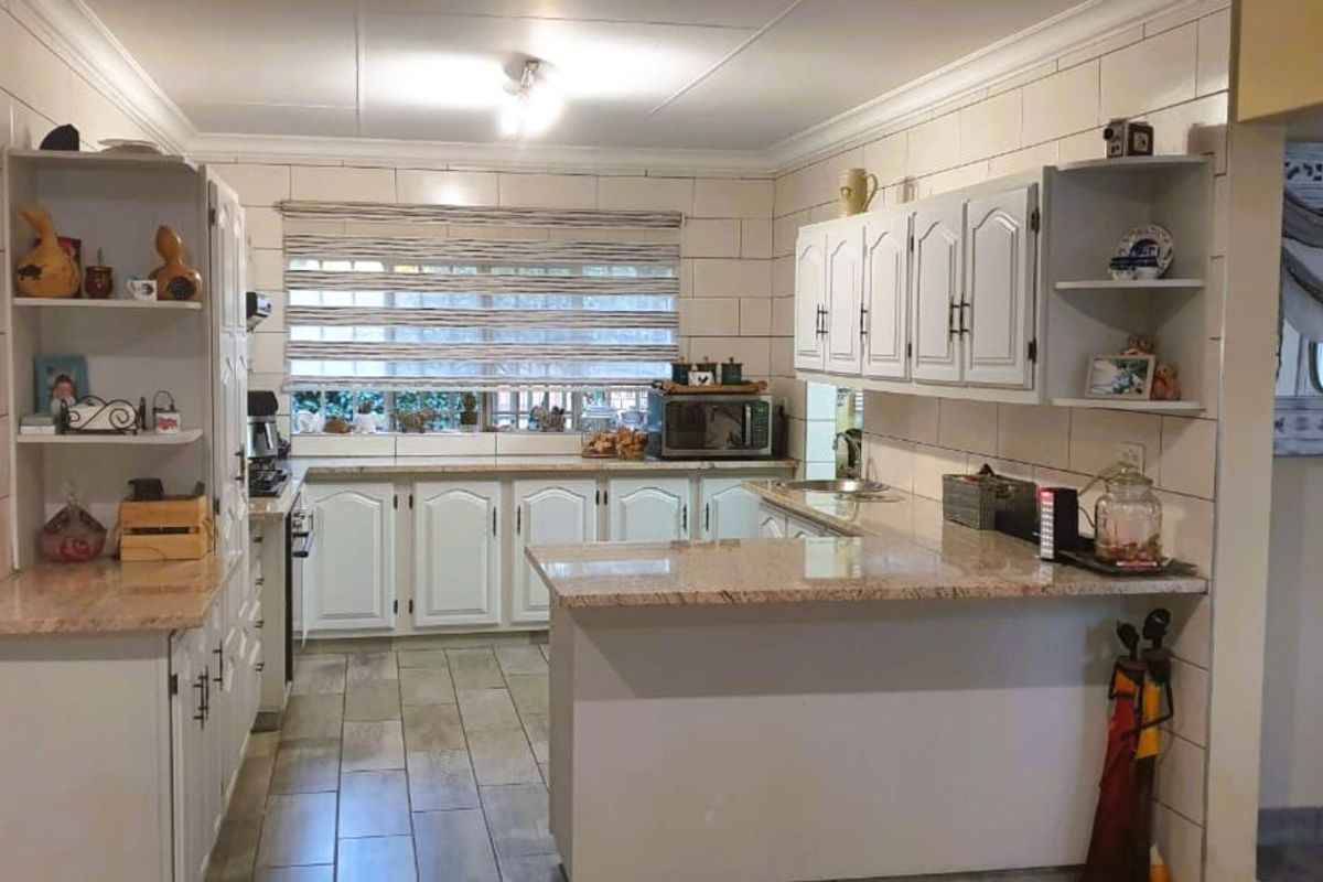 A functional kitchen featuring white cabinetry, granite countertops, tiled walls, and wood-look floor tiles, offering a practical layout for daily meal preparation.