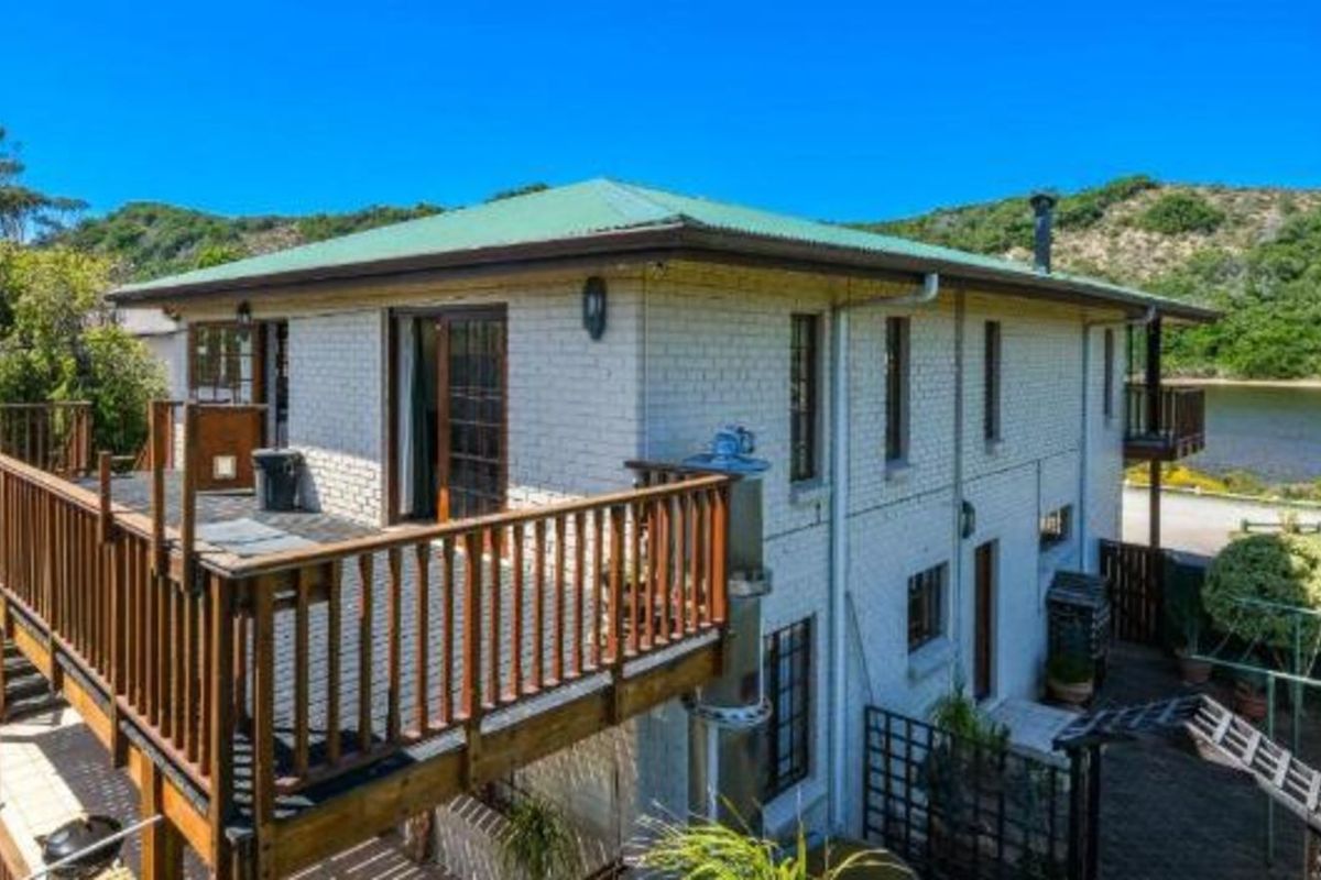 Elevated view of the rear exterior featuring a spacious timber deck, brick facade, and green metal roof overlooking the surrounding landscape.