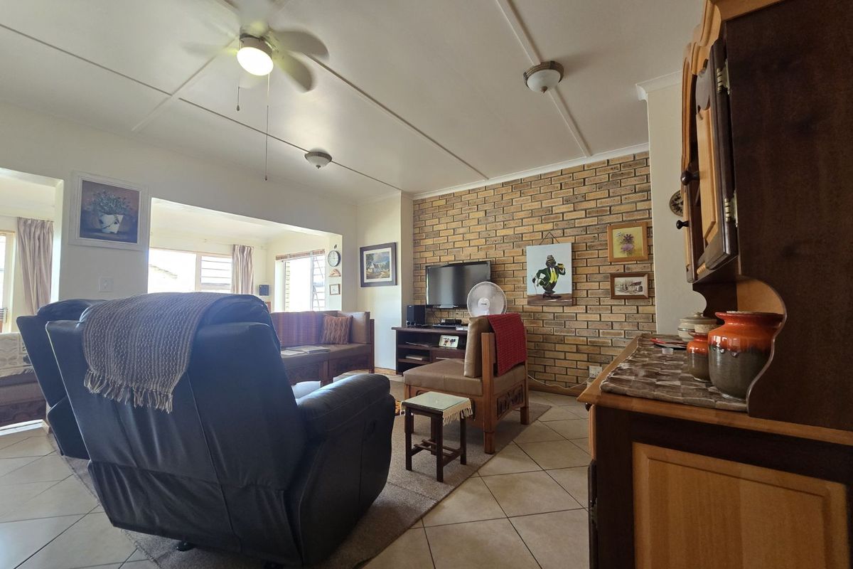 Spacious living room featuring a prominent face-brick feature wall, tiled flooring, and a ceiling fan, offering a comfortable and functional living space.