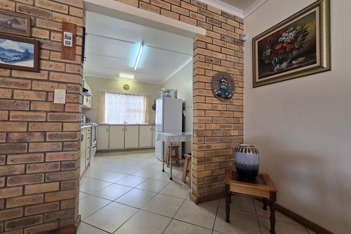 A view from a tiled hallway into a kitchen featuring exposed brick archway detailing, tiled flooring, and built-in cabinetry.