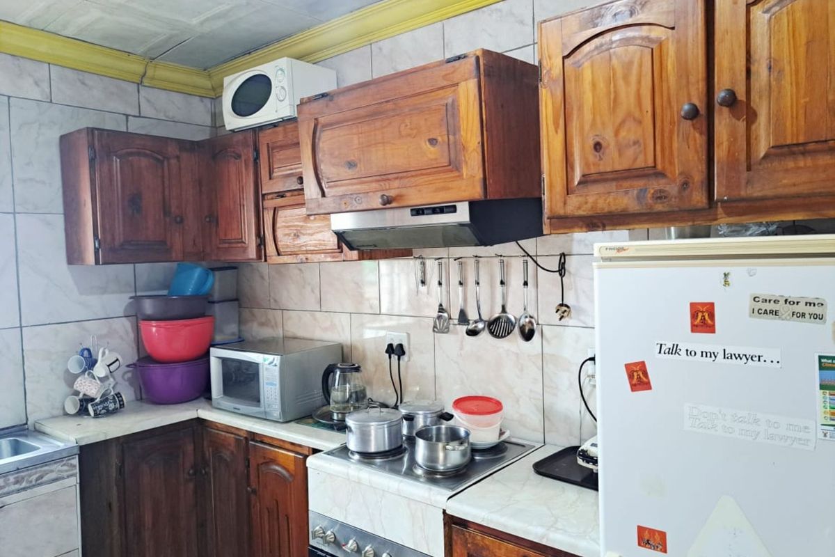 A functional kitchen featuring wooden cabinetry, a tiled backsplash, and a built-in extractor fan, offering a traditional layout with ample storage space.