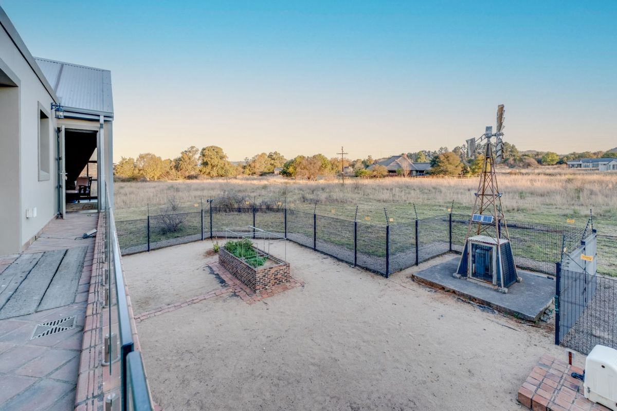 A view of the rear garden area featuring a raised brick planter, a decorative windmill structure, and perimeter security fencing.