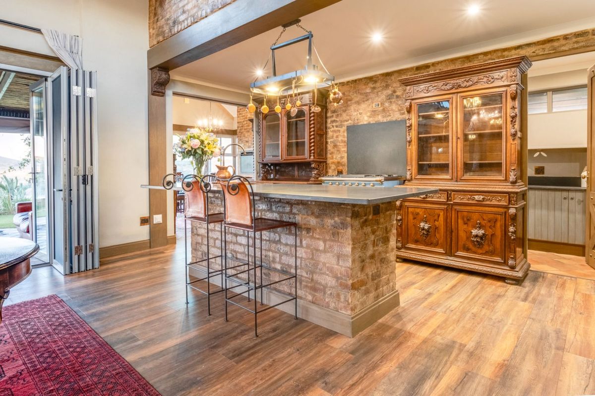 A rustic-style kitchen featuring an exposed brick island, timber flooring, and integrated cabinetry, seamlessly connecting to an outdoor patio area.