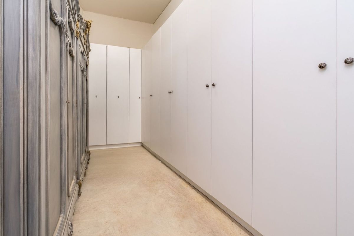 A walk-in dressing area featuring extensive floor-to-ceiling built-in cabinetry with clean white finishes and classic hardware.