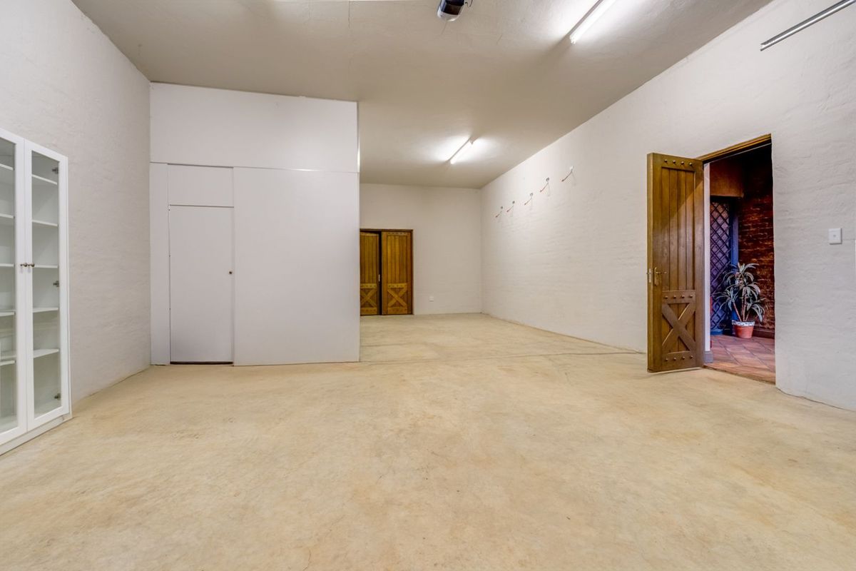 A spacious, empty room featuring white painted brick walls, concrete flooring, and traditional wooden doors, offering a versatile blank canvas.
