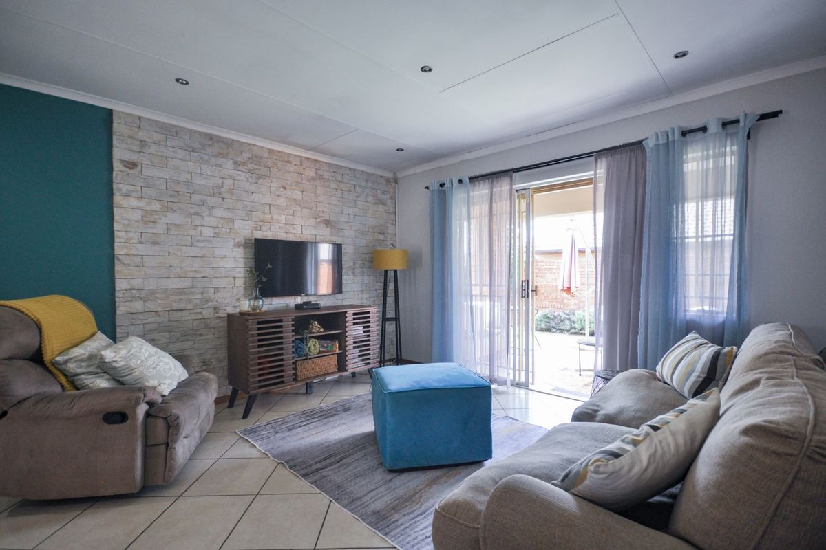 A comfortable living room featuring a textured stone feature wall, tiled flooring, and sliding glass doors that open onto an outdoor patio area.