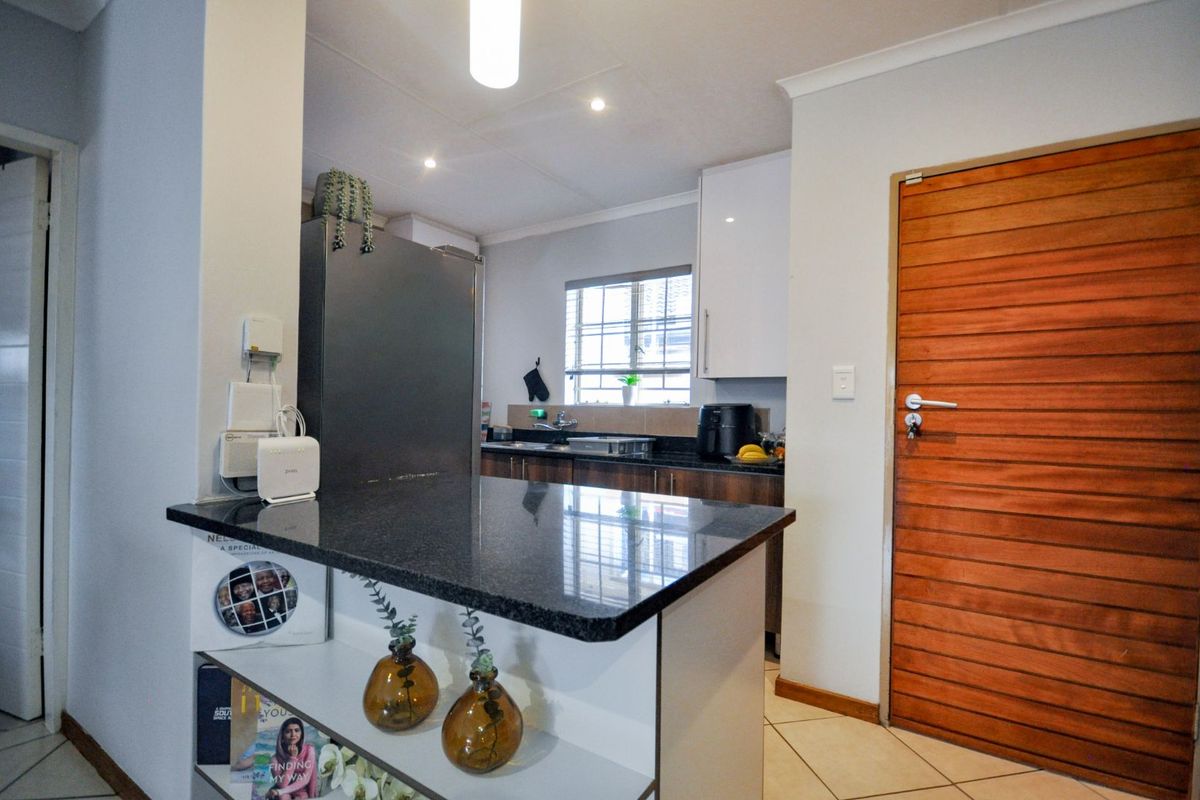 A functional kitchen featuring dark granite countertops, a breakfast bar, white cabinetry, and tiled flooring, adjacent to a wooden entrance door.