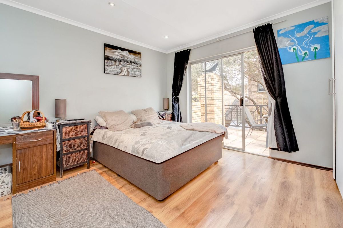 A well-lit bedroom featuring laminate flooring, recessed downlights, and a sliding glass door providing direct access to an outdoor patio area.