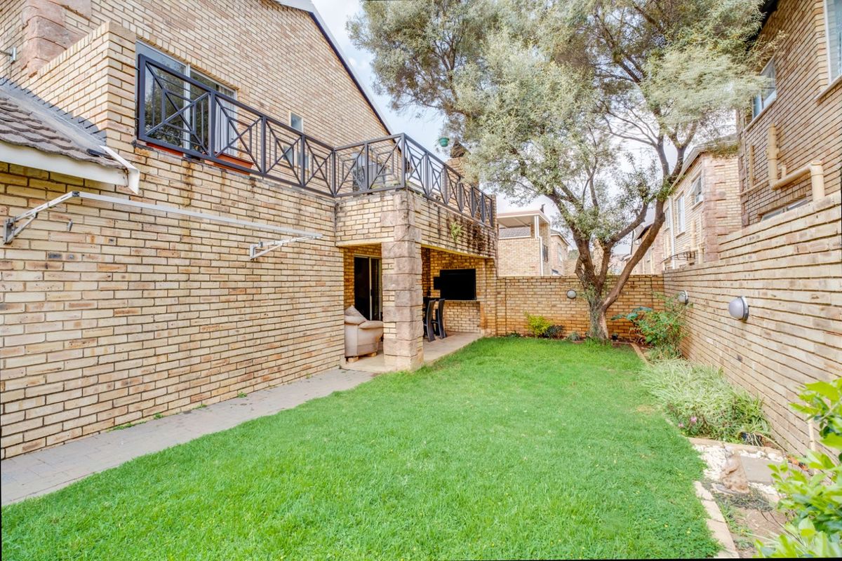 Rear view of the townhouse featuring a private garden, covered patio with built-in braai, and an upper-level balcony with metal railings.