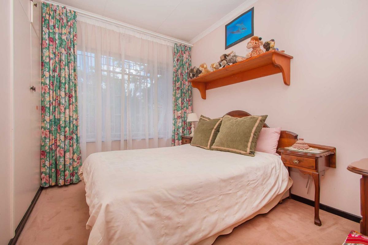 A cozy bedroom featuring built-in cupboards, carpeted flooring, and a window with security bars, offering a functional and comfortable living space.