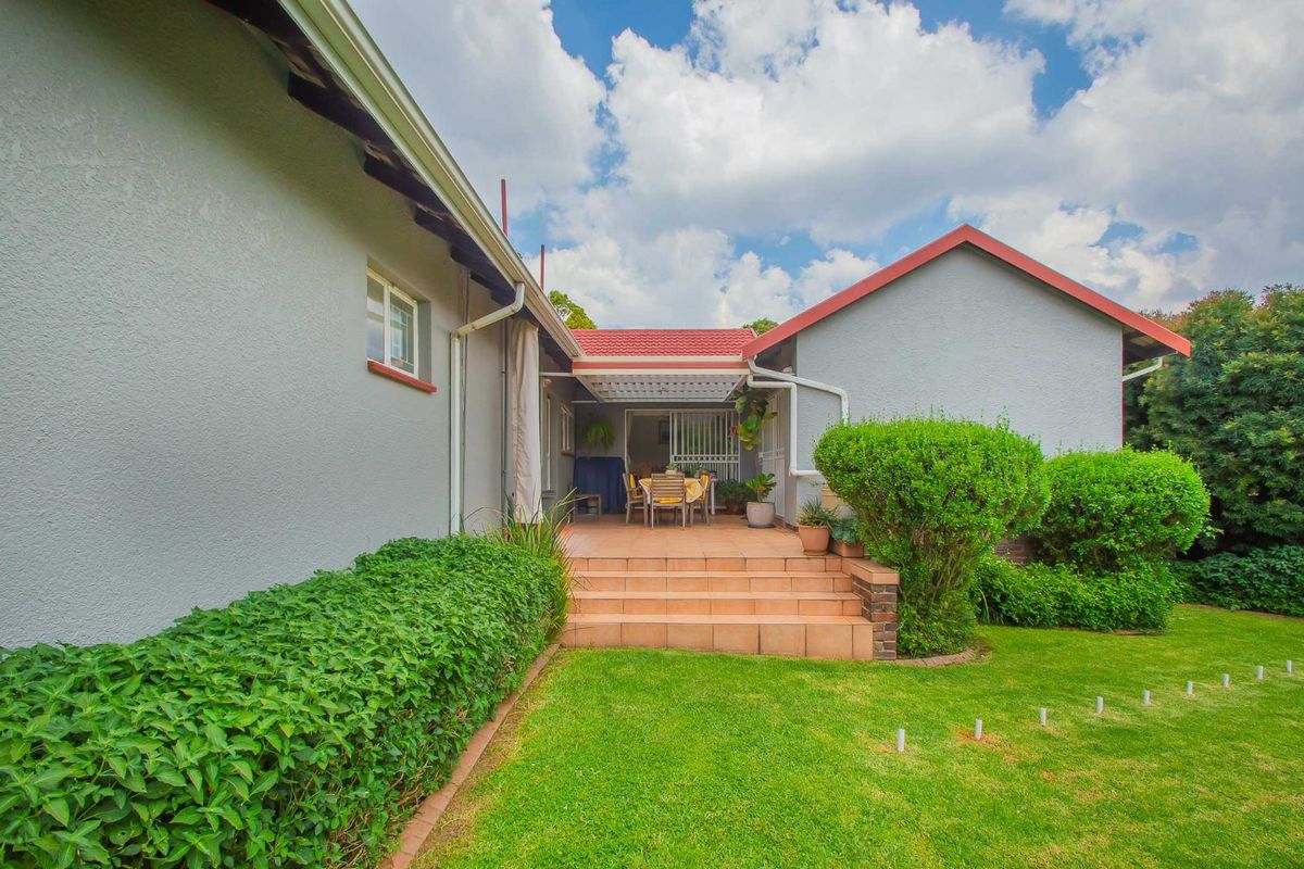A view of the rear exterior featuring a covered patio with tiled steps leading to a well-maintained garden and lawn area.