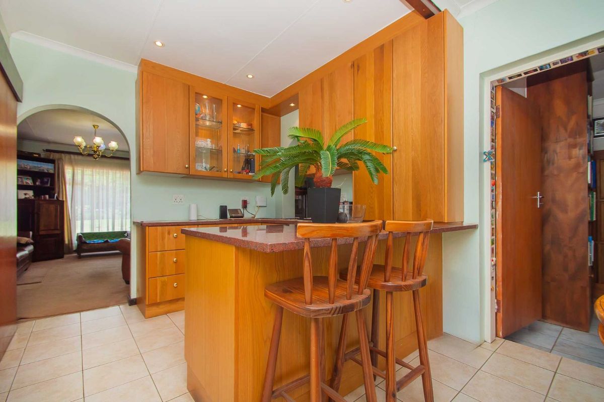A functional kitchen featuring wooden cabinetry, a granite countertop breakfast bar, and tiled flooring, with an adjacent arched entryway leading to the living area.