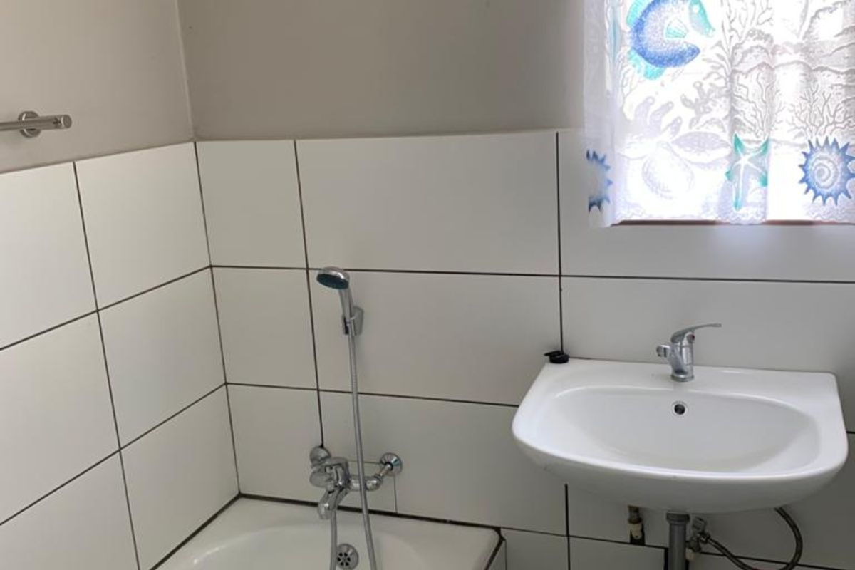 A functional bathroom featuring a white bathtub with a handheld shower mixer and a wall-mounted basin with exposed plumbing.