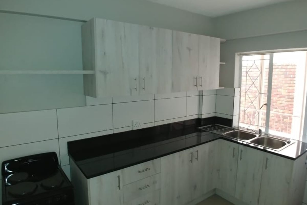 A functional kitchen featuring light wood-grain cabinetry, black countertops, a double-basin sink, and a freestanding stove, complemented by white tiled splashbacks.