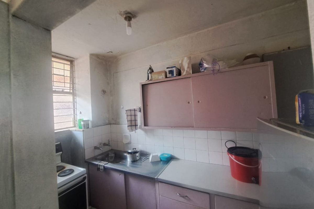 A compact, dated kitchen featuring original cabinetry, a stainless steel sink, and tiled splashbacks, requiring significant renovation and cosmetic updates.