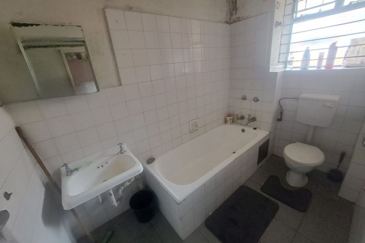 A dated bathroom featuring a standard bathtub, wall-mounted basin, and toilet, requiring significant renovation and cosmetic updates to restore functionality and appeal.