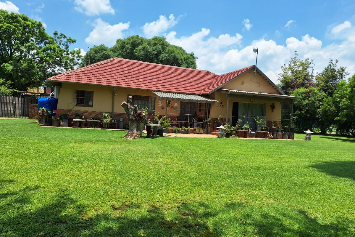 A view of the rear elevation of the house, featuring a tiled roof, covered patio area, and a large, well-maintained lawn.