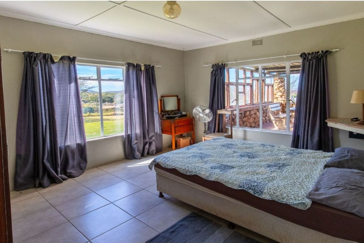A spacious bedroom featuring large windows with natural light, tiled flooring, and direct views of the surrounding farm landscape.