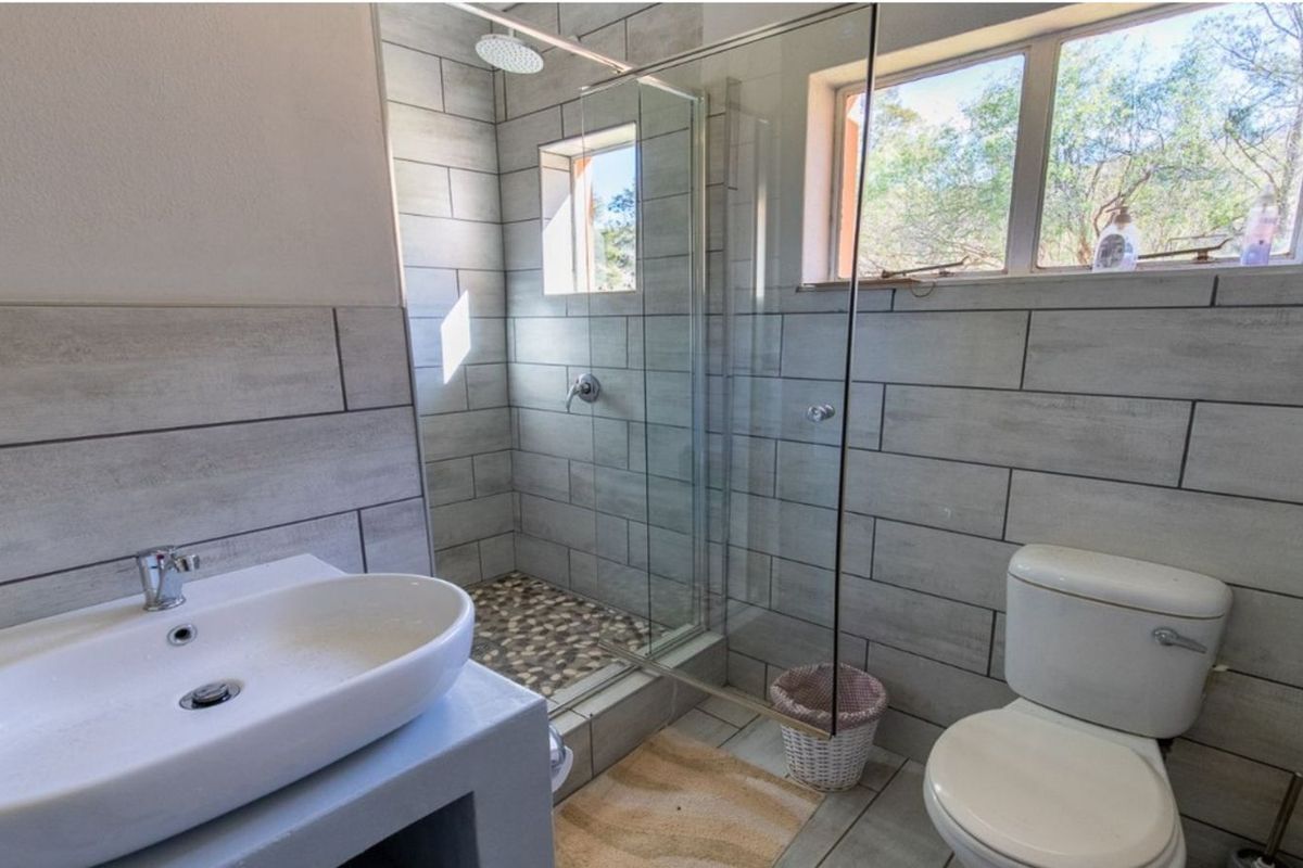 A modern bathroom featuring a walk-in shower with a pebble-stone floor, a vessel sink on a vanity, and a toilet.