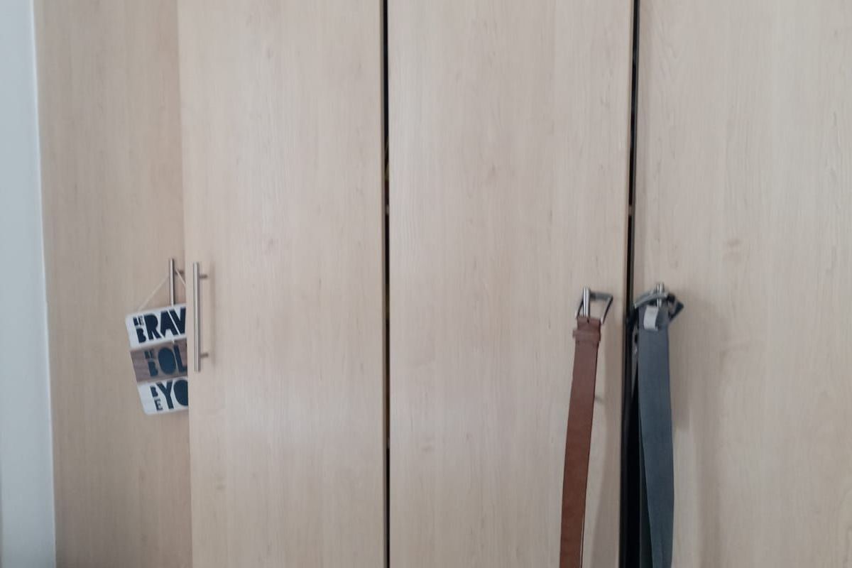 A bedroom featuring built-in light wood-finish cupboards with modern metal handles.