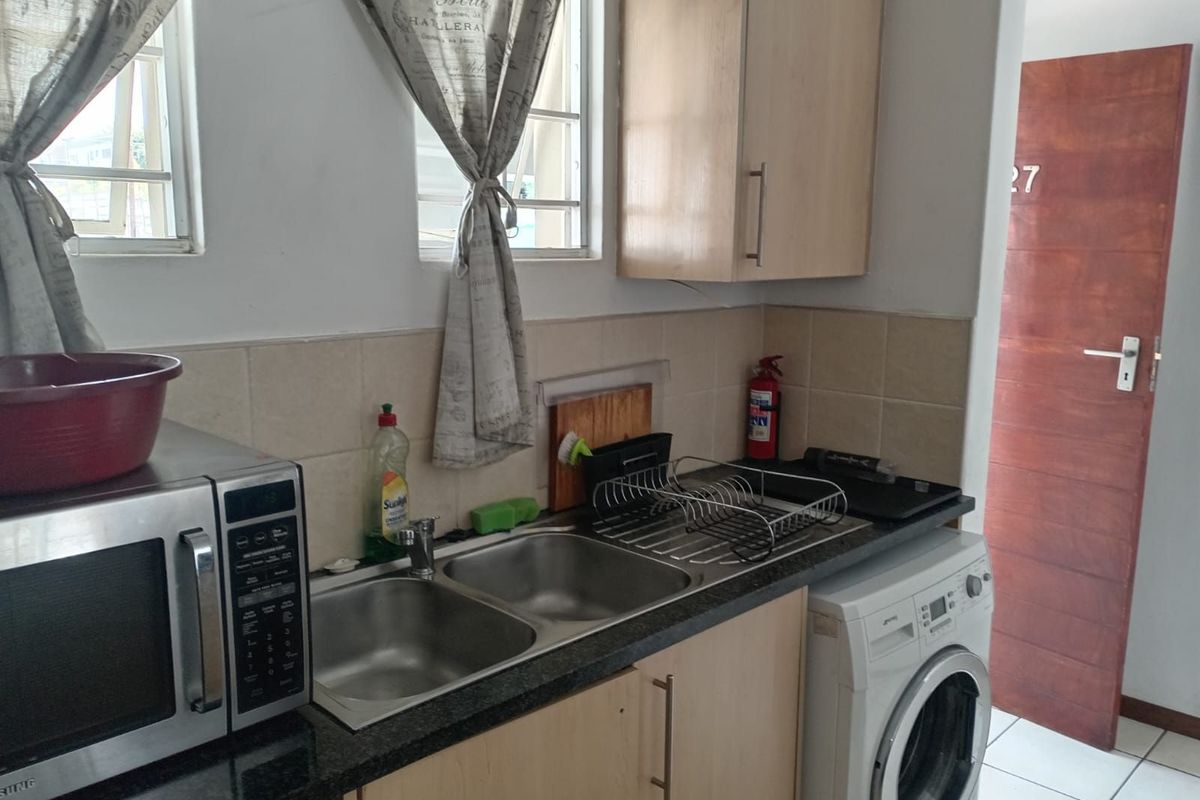 A functional kitchen area featuring a double stainless steel sink, laminate cabinetry, and space for a front-loading washing machine.