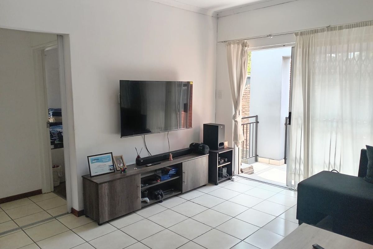 A living room featuring tiled flooring and a sliding glass door leading to a balcony, providing natural light and access to outdoor space.