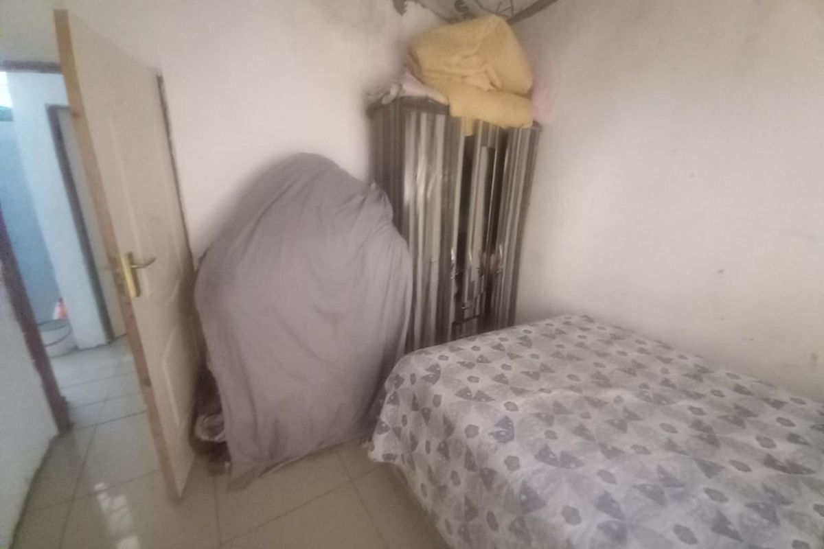 A small bedroom featuring tiled flooring and a standard door, currently showing signs of wear and requiring maintenance to the walls and ceiling.