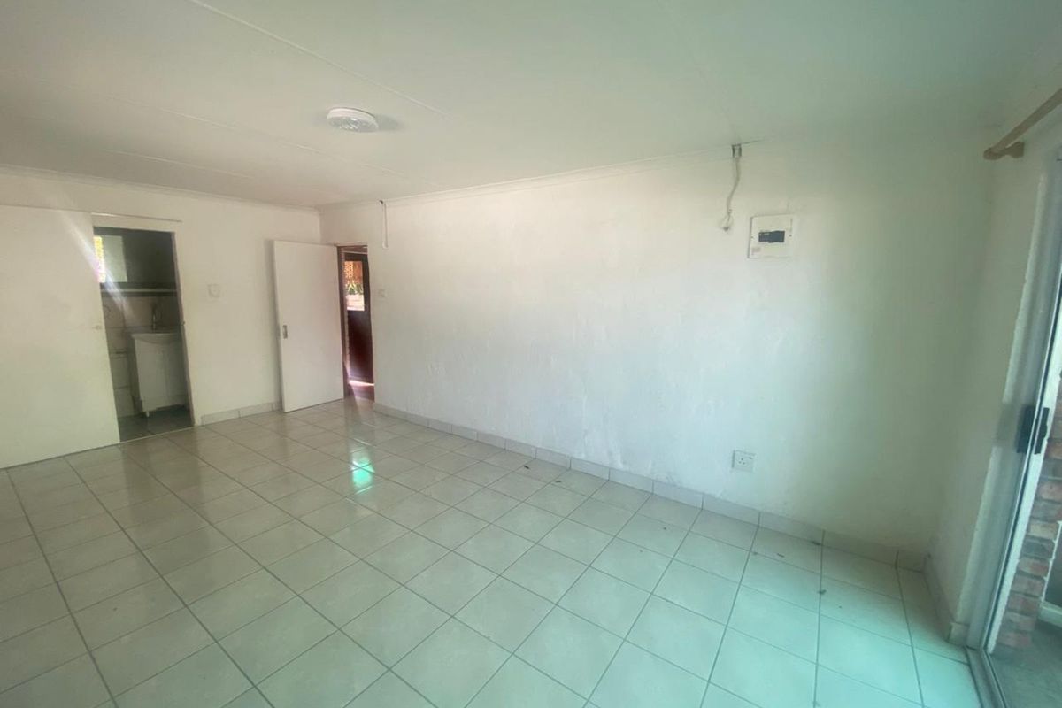 An empty living area featuring tiled flooring, neutral walls, and direct access to an adjacent room and exterior patio.