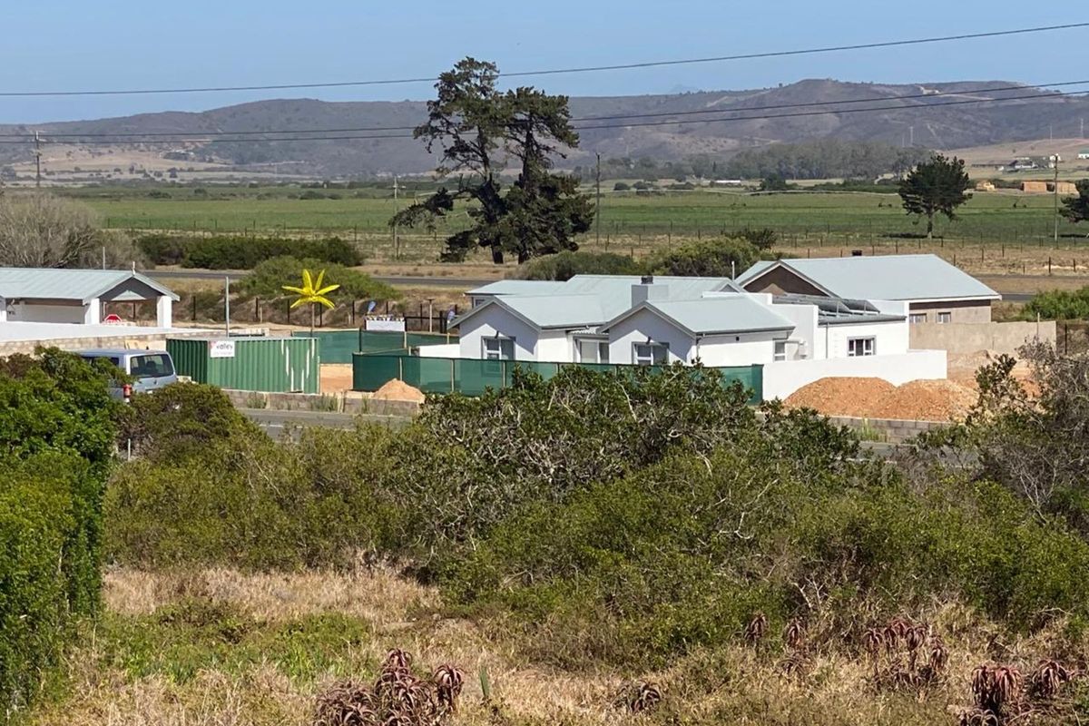 An elevated view of a residential property under construction, featuring white buildings with metal roofs set against a rural landscape.