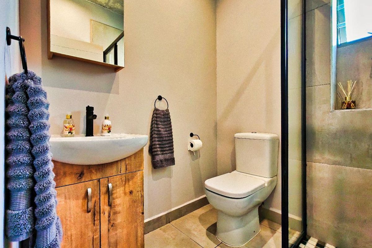 Modern bathroom featuring a wooden vanity with a vessel sink, black fixtures, a wall-mounted mirror, and a glass-enclosed shower with tiled flooring.