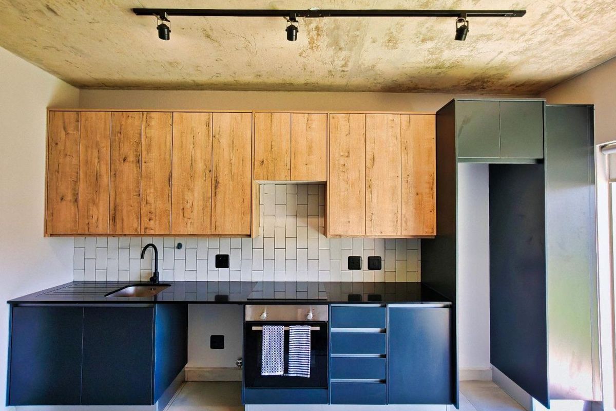 Modern kitchen featuring wood-grain upper cabinetry, dark lower cabinets, black stone countertops, subway tile backsplash, and a built-in oven with hob.