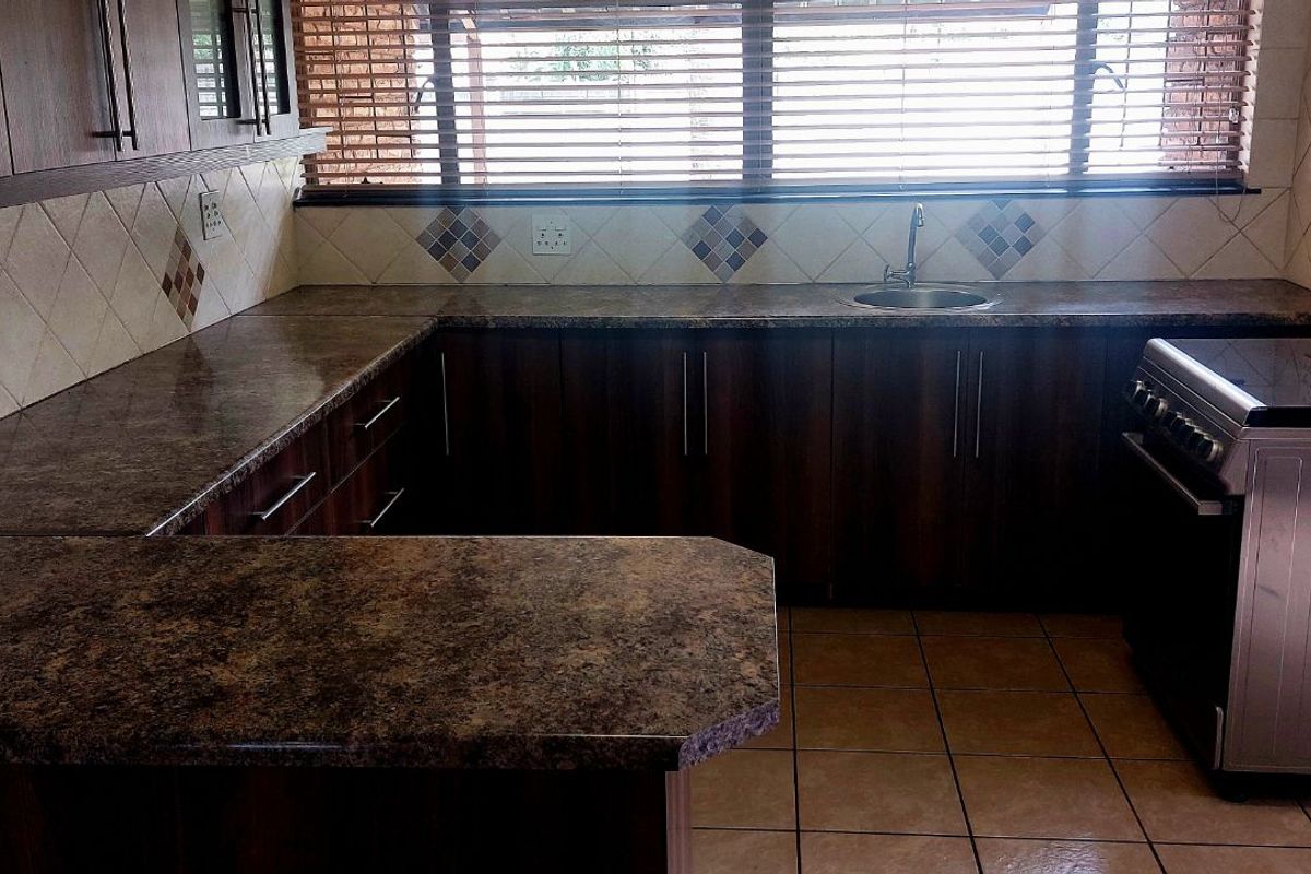 A functional kitchen featuring dark wood cabinetry, laminate countertops, tiled backsplash, and a freestanding stove with an integrated sink.
