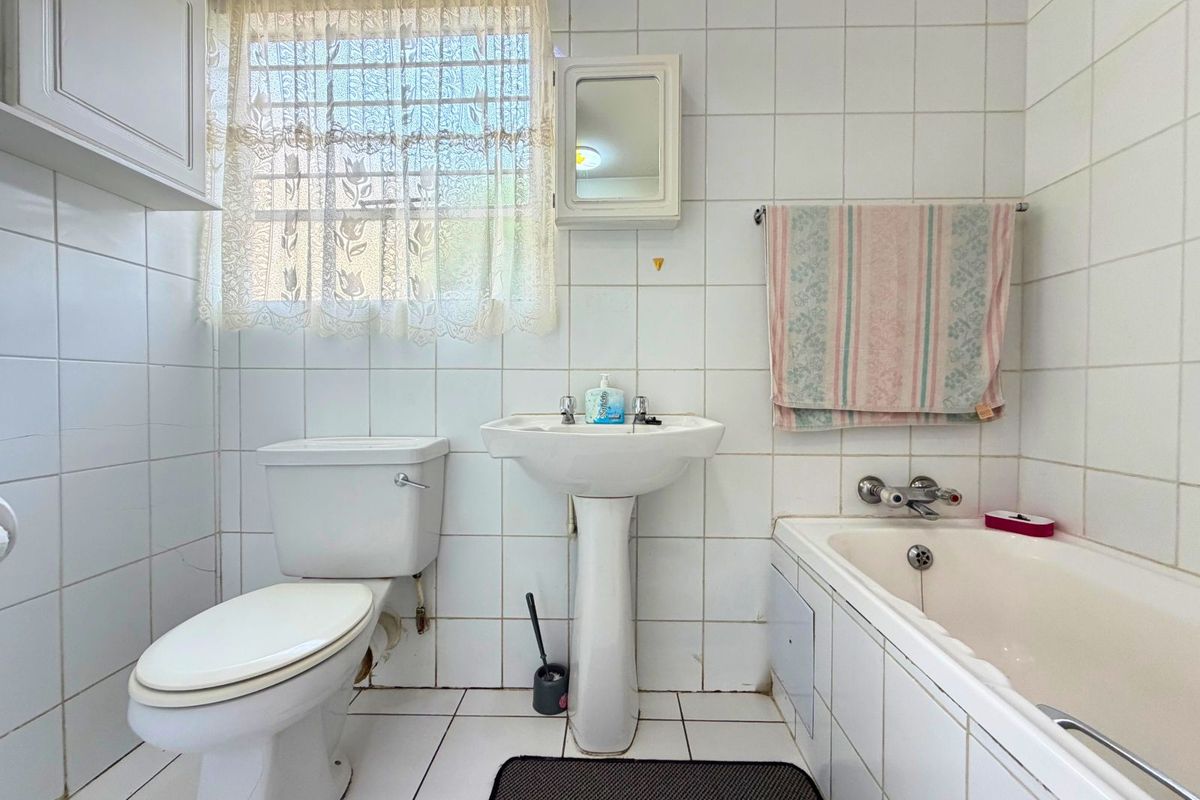 A functional bathroom featuring a pedestal sink, standard toilet, and a built-in bathtub with wall-to-wall white tiling.