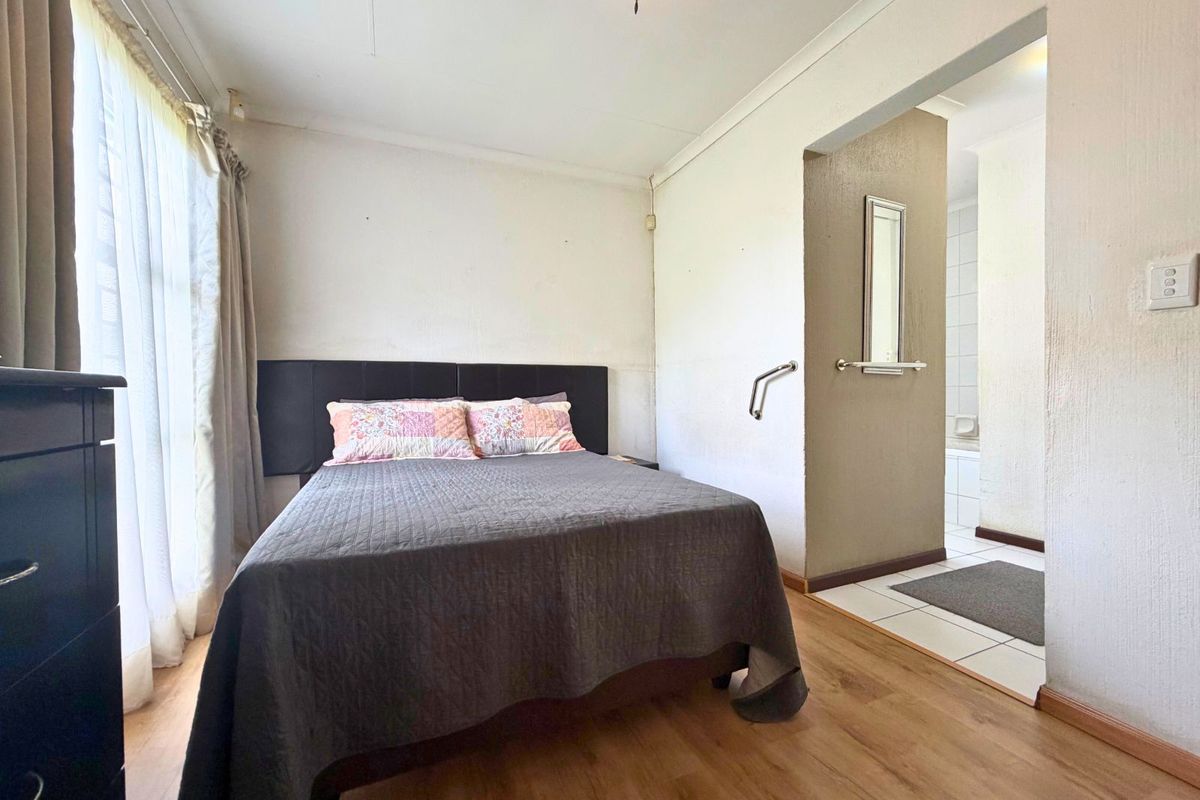 A bedroom featuring laminate flooring and an en-suite bathroom access, with neutral wall finishes and a built-in headboard.