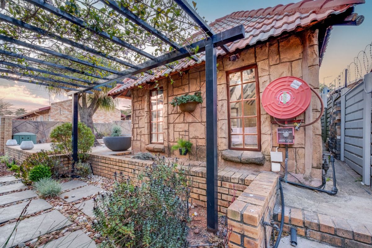 A rear exterior view of the townhouse featuring a stone-clad facade, a metal pergola structure, and a paved garden area with a fire hose reel.