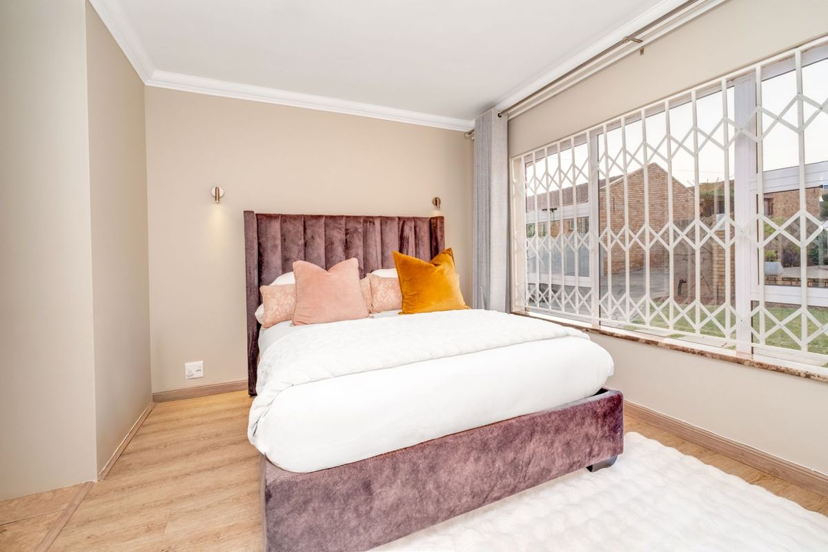 A well-maintained bedroom featuring light wood-look flooring, neutral wall tones, and a large window fitted with a white security gate.