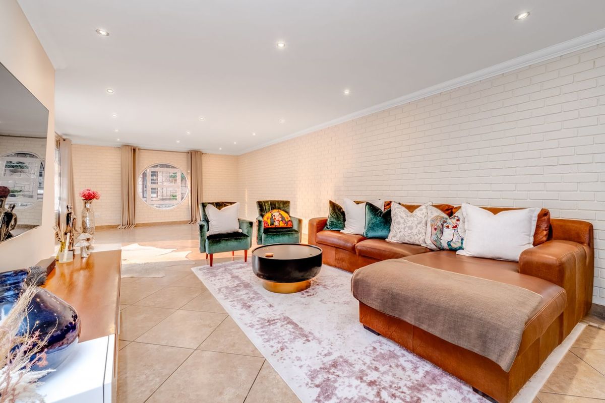 Spacious living room featuring a distinctive circular window, recessed ceiling lighting, and a textured white brick feature wall with tiled flooring.