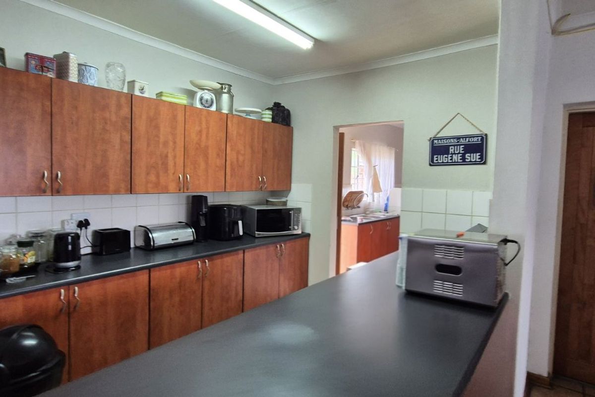 A functional kitchen featuring wood-finish cabinetry, dark countertops, and a breakfast bar, with an adjacent scullery area visible through the doorway.