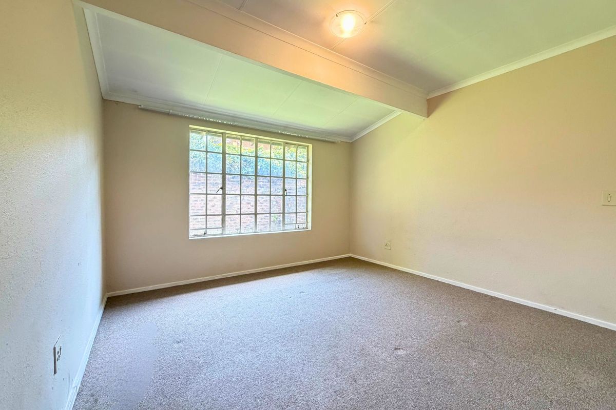 A vacant bedroom featuring neutral wall tones, carpeted flooring, and a large window providing natural light.