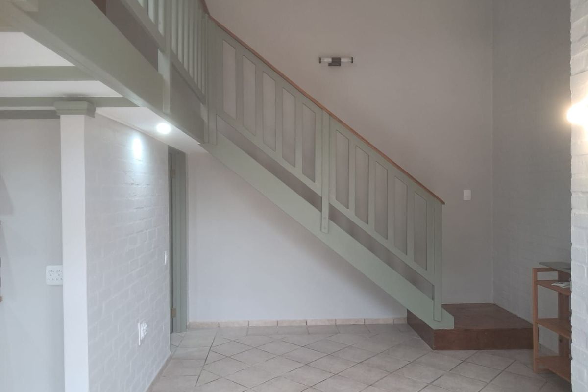 Interior view of a living area featuring a painted wooden staircase with balustrade leading to a mezzanine level, finished with tiled flooring.