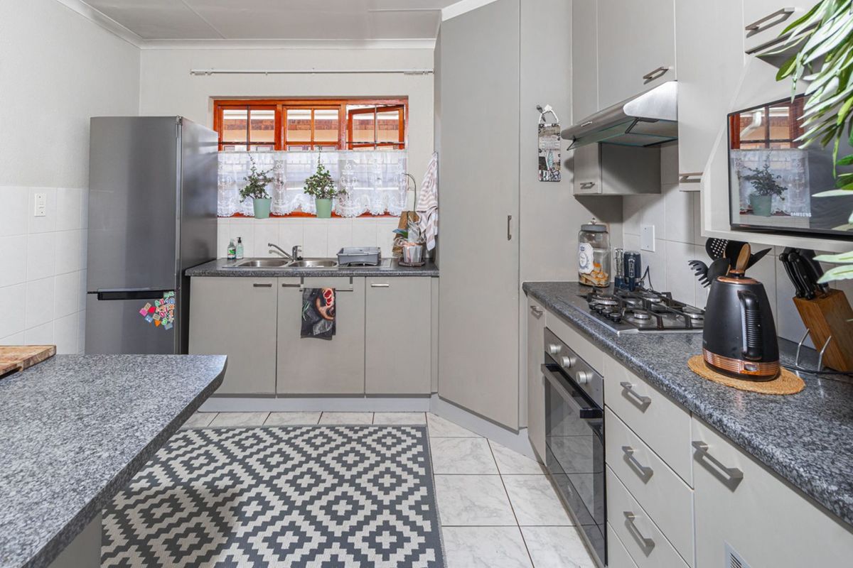 A functional kitchen featuring grey cabinetry, granite-look countertops, a built-in oven, gas hob, extractor fan, and tiled flooring.