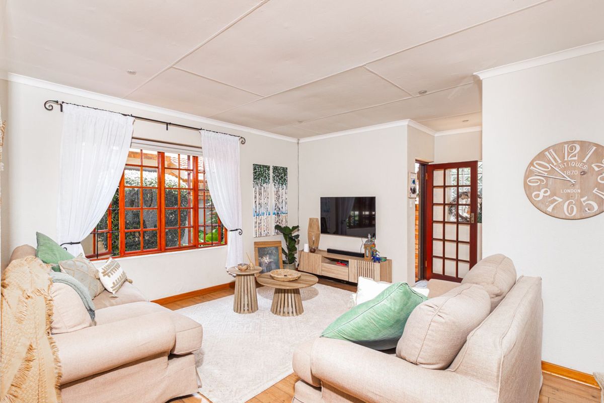 A comfortable living room featuring timber flooring, large windows with wooden frames, and a classic glass-paneled door leading to adjacent spaces.