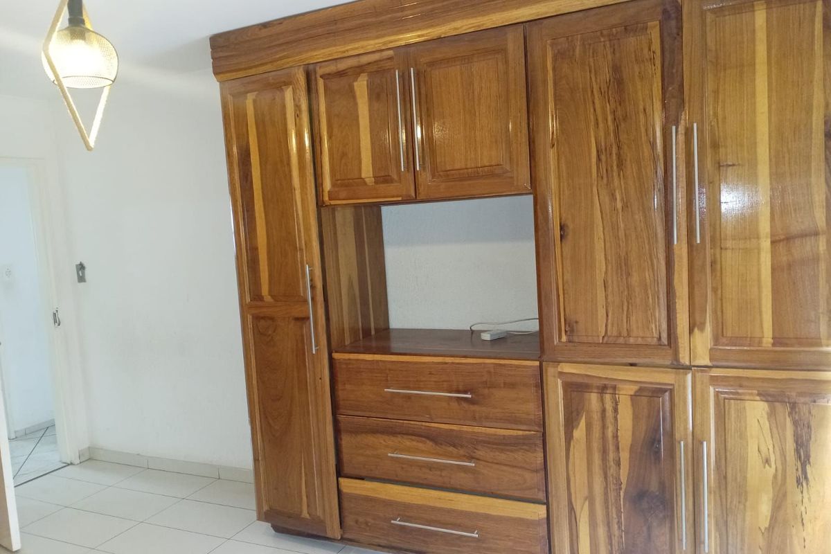 A bedroom featuring large, built-in wooden cabinetry with integrated storage drawers and shelving, set against a tiled floor.