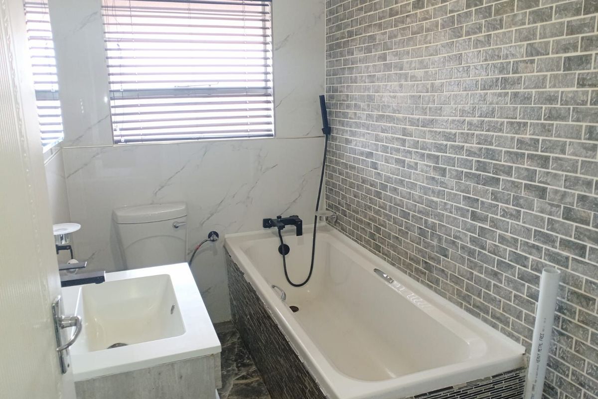 Modern bathroom featuring a built-in bathtub with a handheld shower mixer, a vanity basin, and decorative tiled wall finishes.