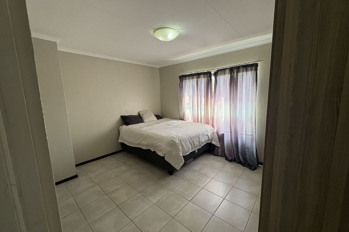 A functional bedroom featuring neutral wall finishes, tiled flooring, and a window with curtain tracks.
