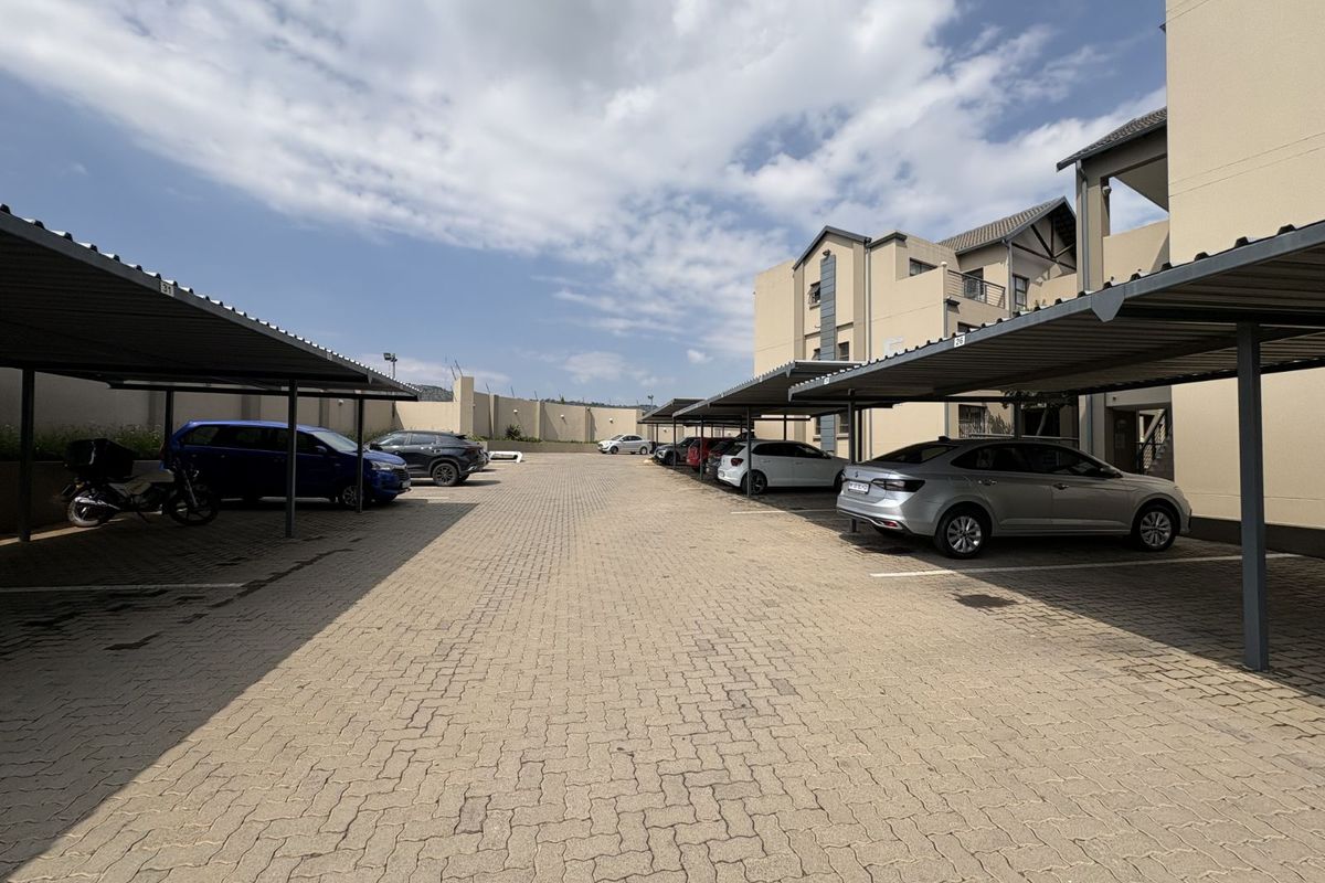 A paved parking area featuring covered carports for residents, situated within a well-maintained apartment complex.