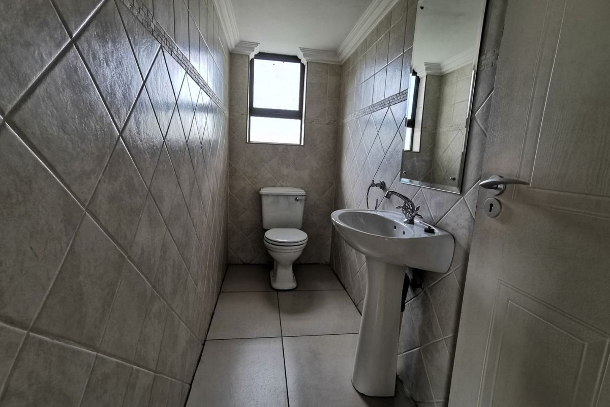 A compact guest bathroom featuring floor-to-ceiling ceramic wall tiles, a pedestal basin, and a standard toilet.