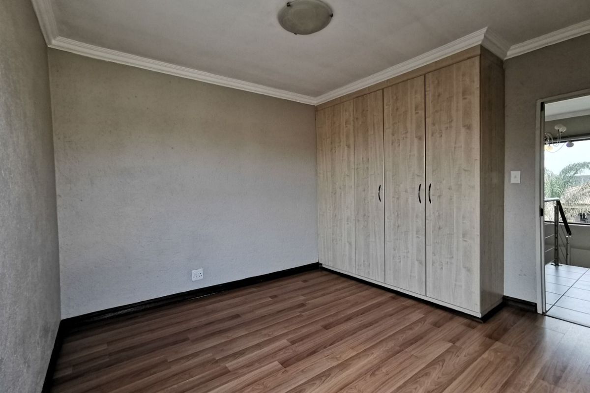 A bright, empty bedroom featuring built-in wooden wardrobes, laminate flooring, and crown molding, offering a clean and versatile space.